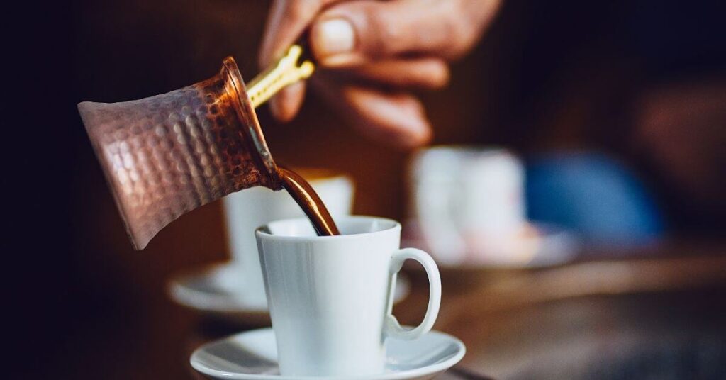 A Person pouring Turkish coffee in a white coffee cup 