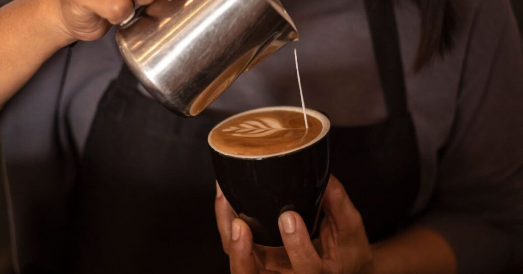 A person pouring coffee on a coffee cup to create a flower 